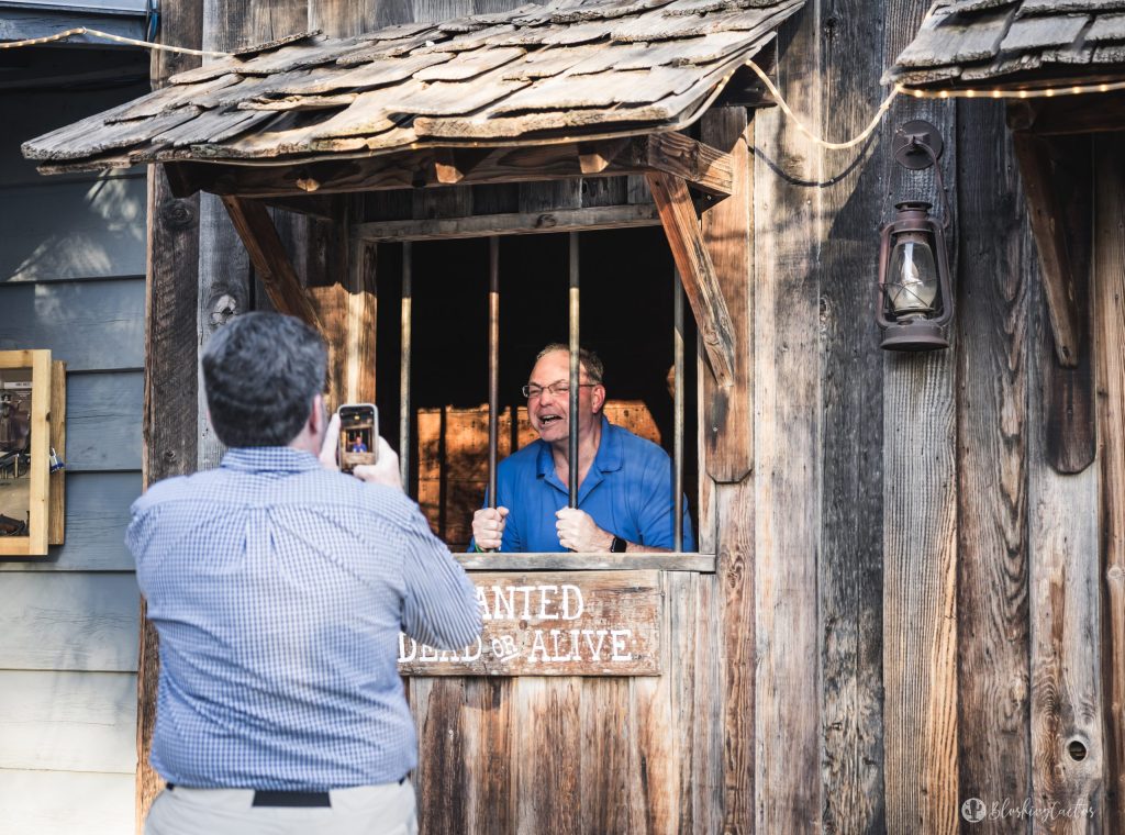 Man posing behind pretend jail bars as another takes a photo.