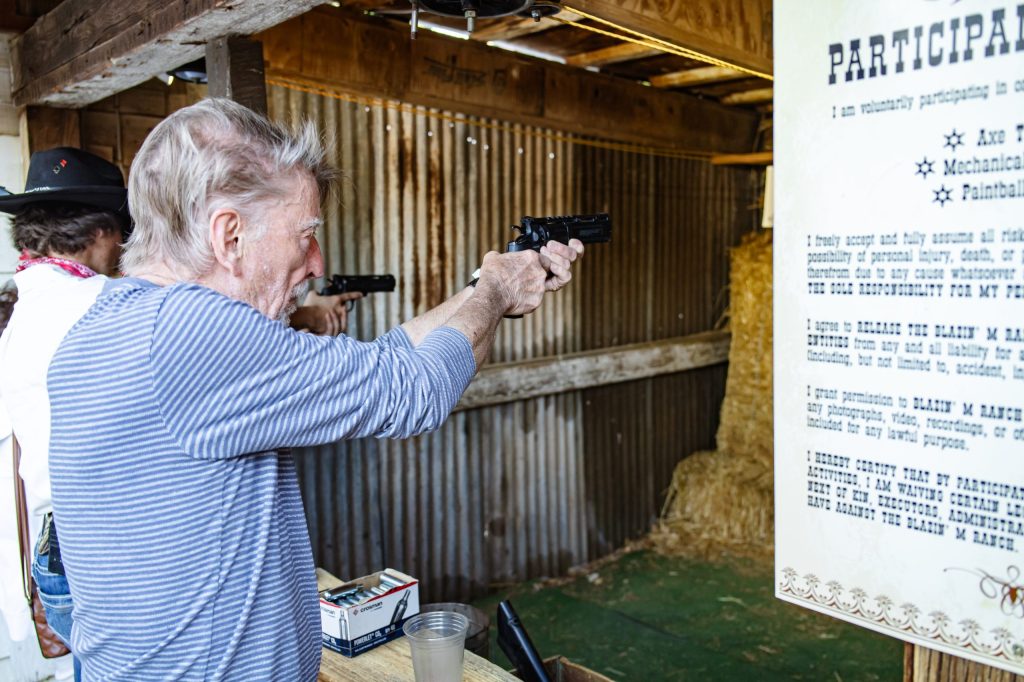 Two people aiming pistols at a shooting range with a wooden backdrop.