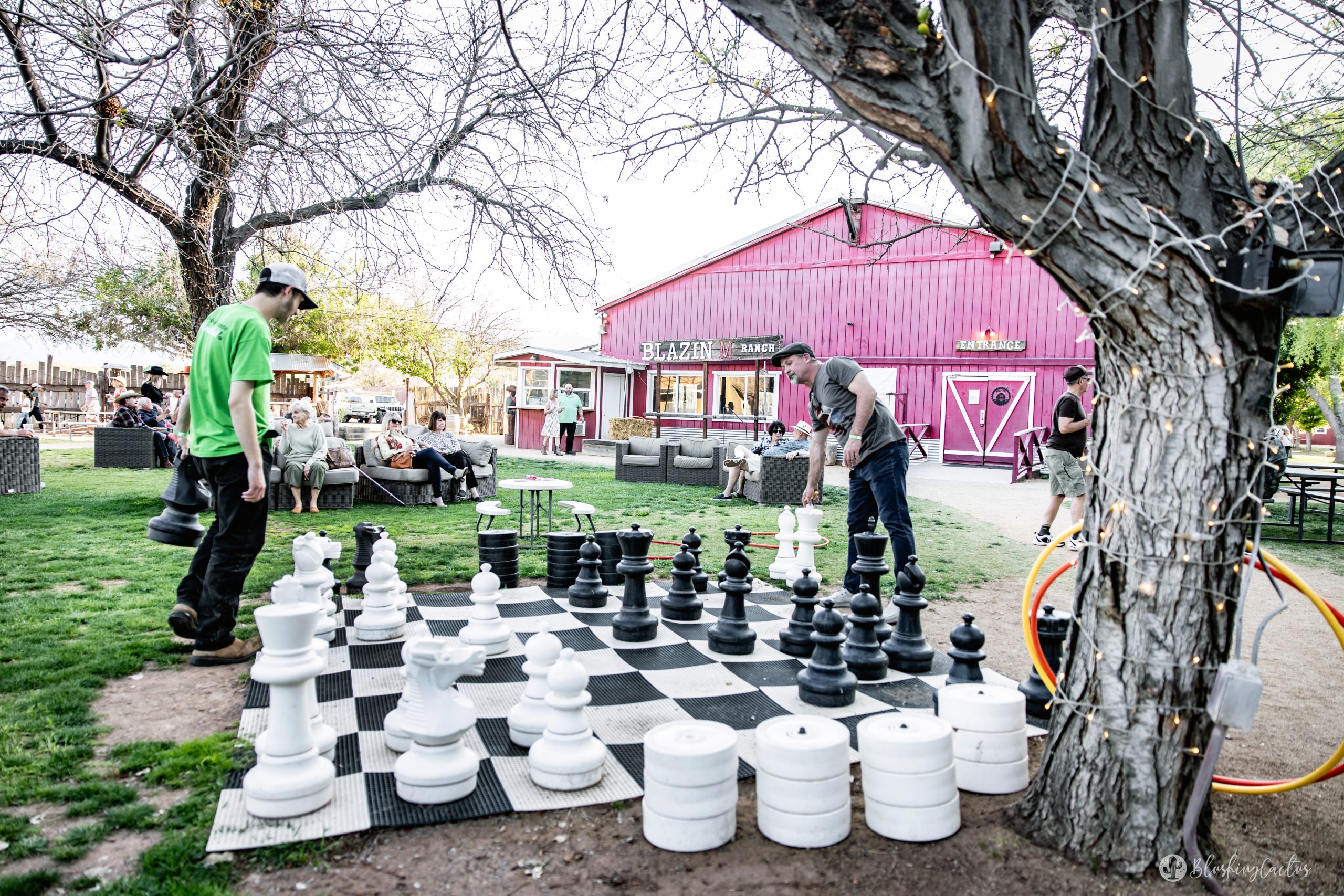 People playing giant chess outdoors near a red building.
