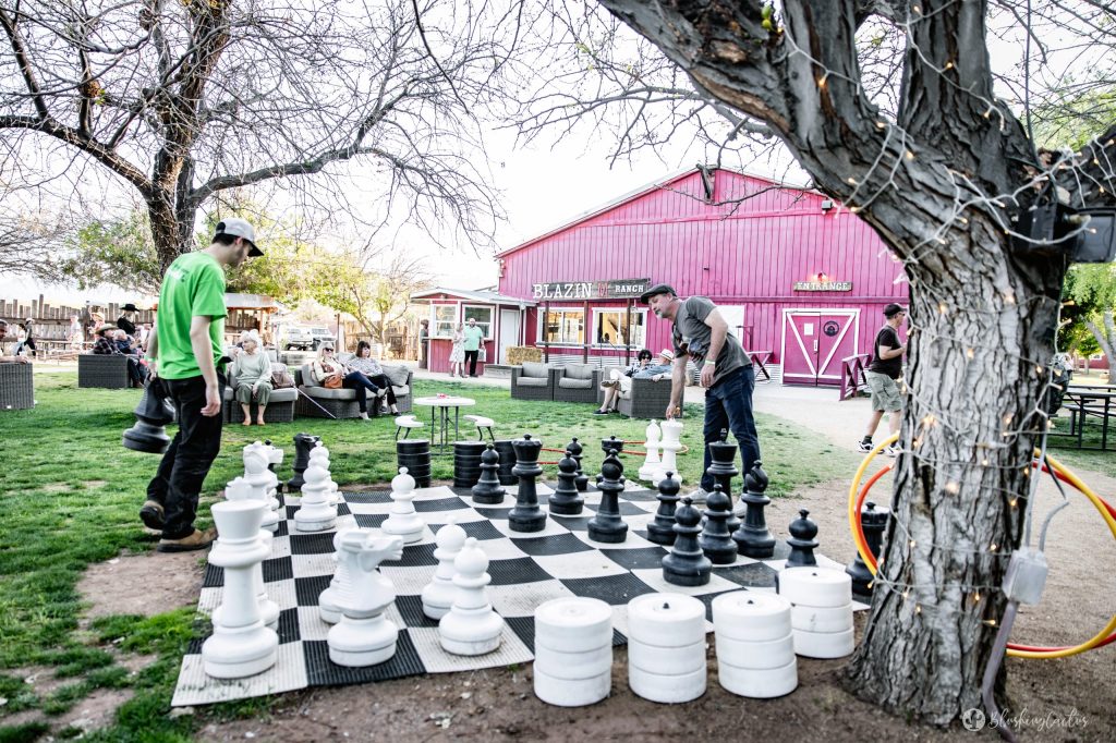 People playing giant chess outdoors near a red building.