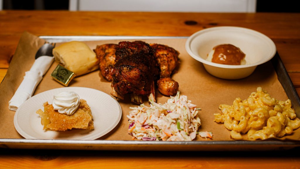 Tray with rotisserie chicken, mac and cheese, coleslaw, bread roll, pie slice, and butter.