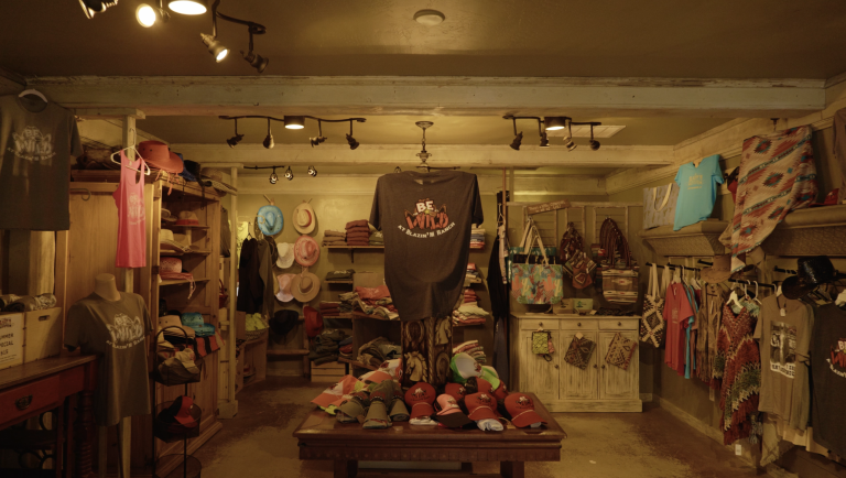 Rustic shop interior with clothes, hats, and accessories displayed on shelves and a table.