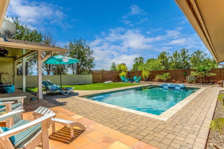 Backyard with swimming pool, lounge chairs, and umbrella under a clear blue sky.