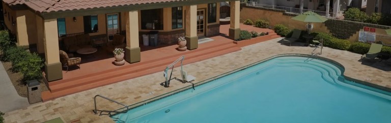Outdoor pool with diving board and adjacent patio with seating area.
