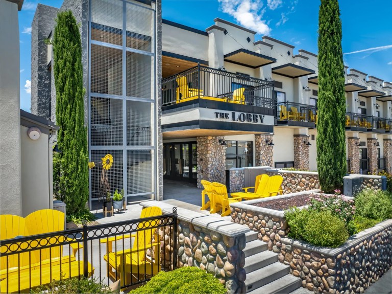 Modern hotel exterior with yellow chairs and stone accents.