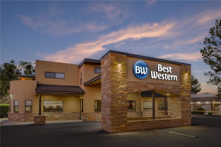 Exterior of a Best Western hotel at dusk with lit signage and a cloudy sky.