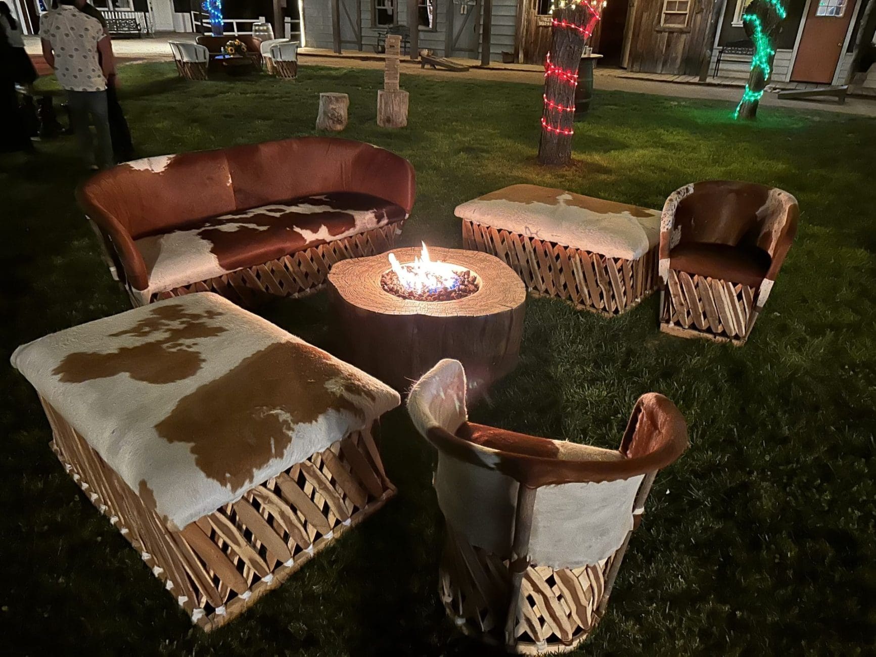 Outdoor seating with cowhide chairs and table around fire pit at night.