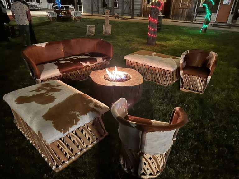 Outdoor seating with cowhide chairs and table around fire pit at night.