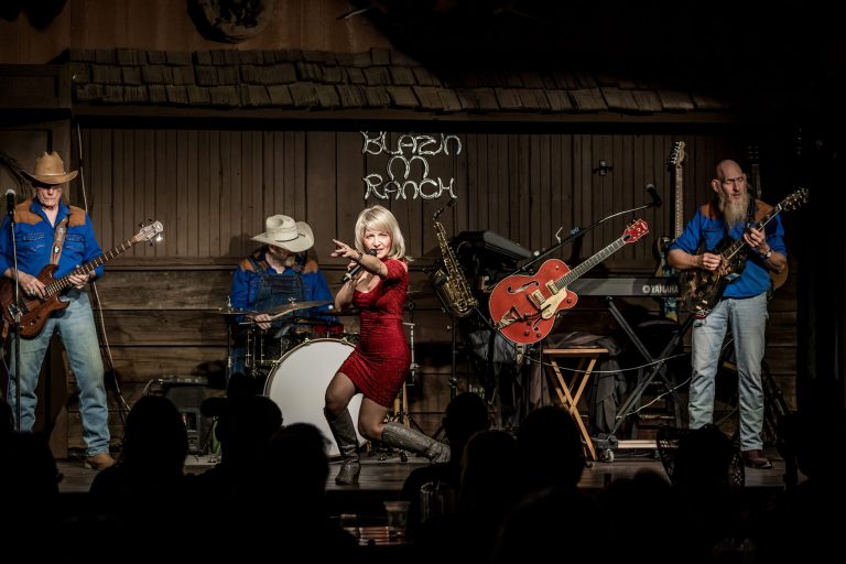 Band performing on stage with a woman singing, guitarists, and drummer.