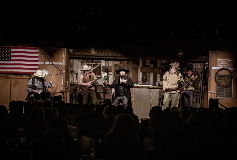 Band performing on stage with an American flag and western decor in background.