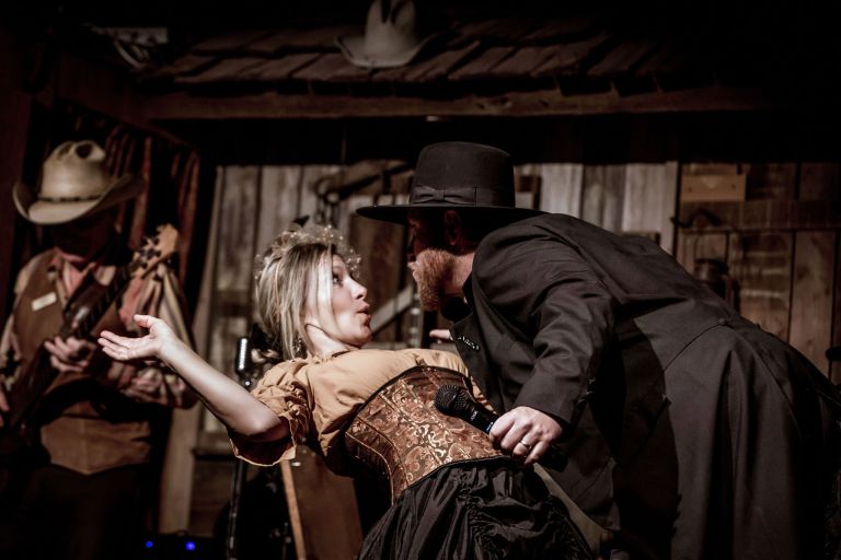 Woman and man in Western attire performing on stage with guitar player.