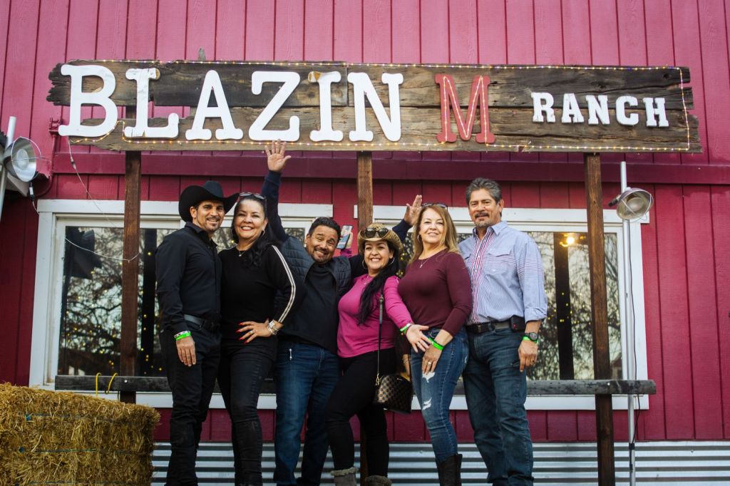 Group of six people smiling under 'Blazin M Ranch' sign.