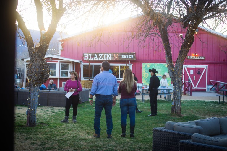 People standing outside a red barn named Blazin Ranch at sunset.