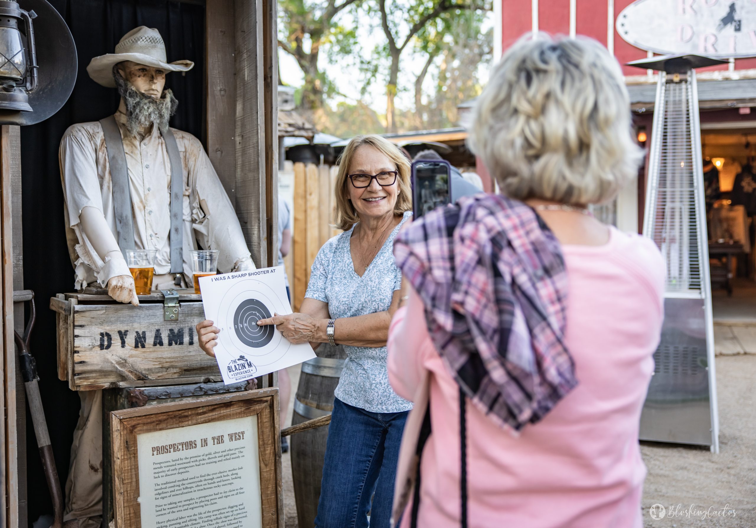 Woman poses with a Wild West target sign, another woman takes a photo outside a Western-themed store.