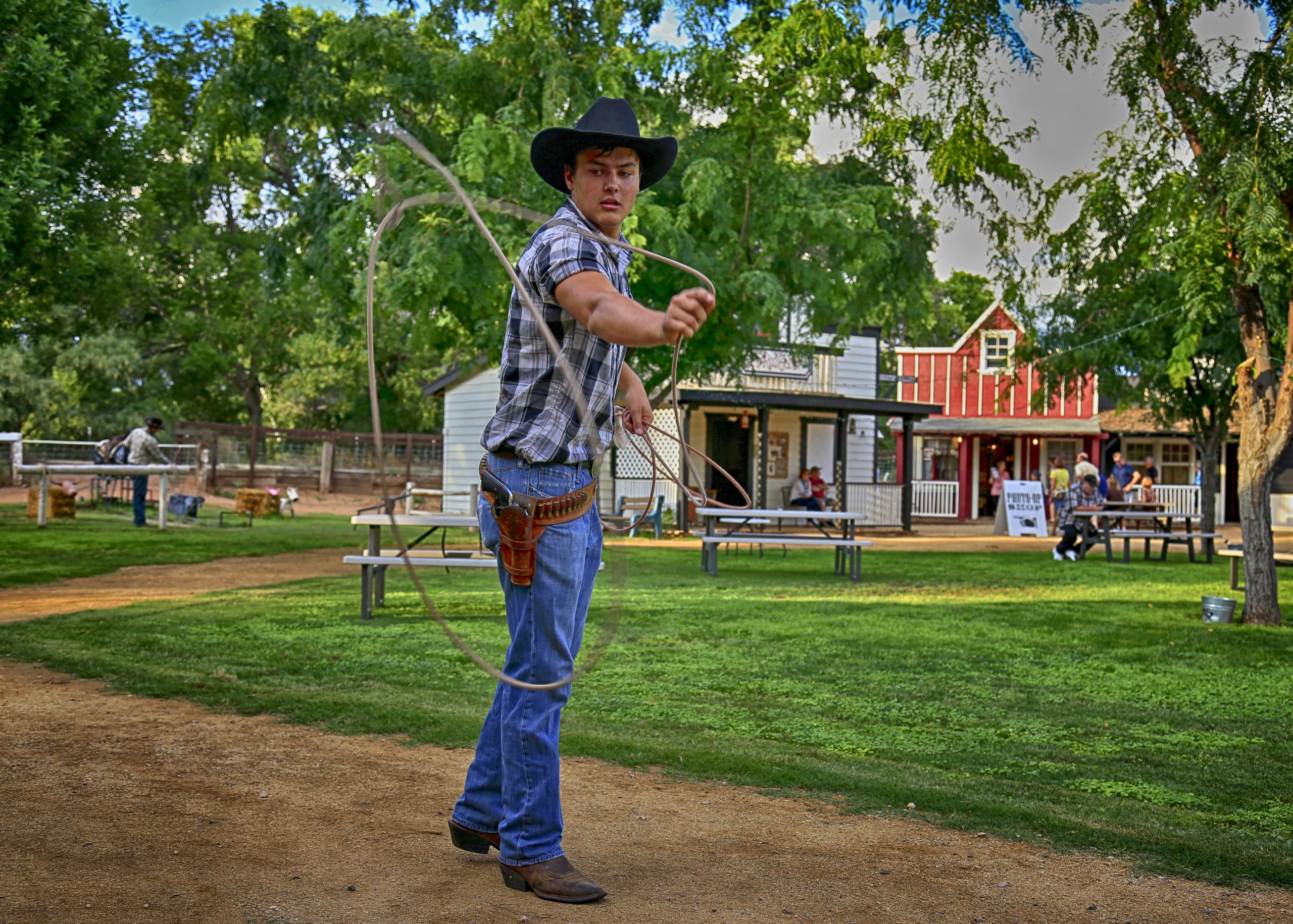 Cowboy in a hat performing lasso trick in a park setting.